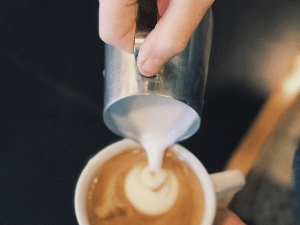 A person pouring cream into a cup of coffee.
