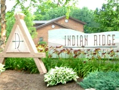 Visitors can enjoy the sign for Indian Ridge nestled amidst lush bushes and towering trees near Oxford attractions.