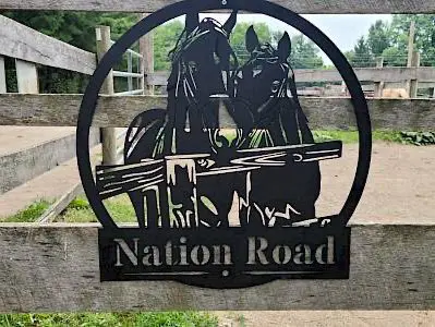 A metal sign featuring two horses that says "Nation Road," a delightful addition to any ensemble.