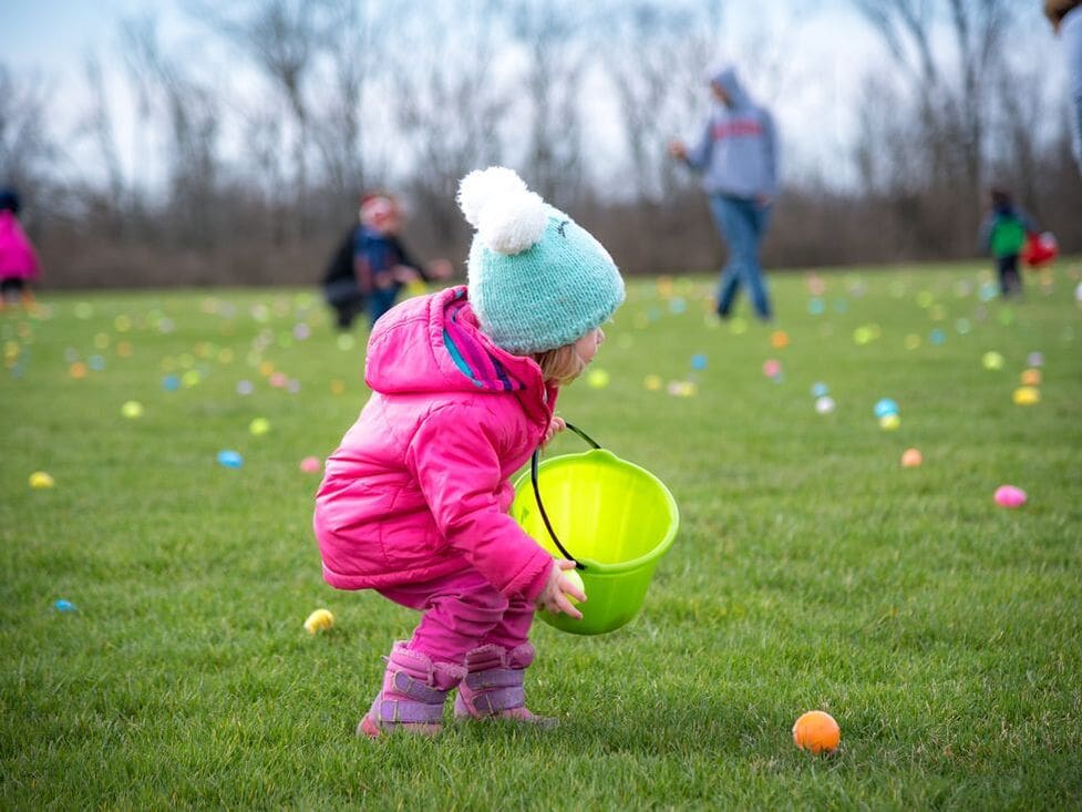 A little girl picking up easter eggs in a grassy field.