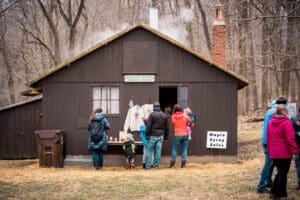 People outside the sugar house tasting maple syrup samples.