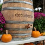 OXtoberfest wooden barrel centered with purple mums and mini pumpkins