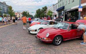 Red Porsche and crowd on brick street.