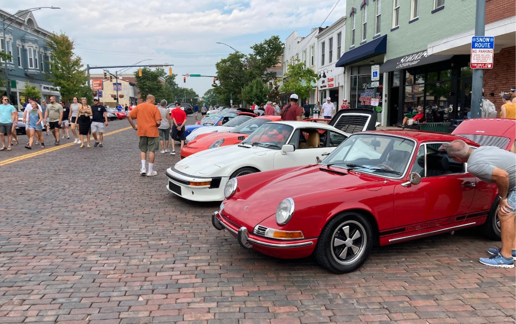 Red Porsche and crowd on brick street.