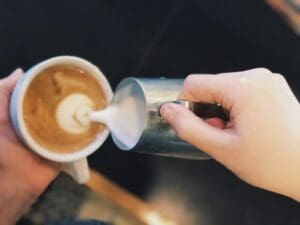 A person pouring cream into a coffee cup.