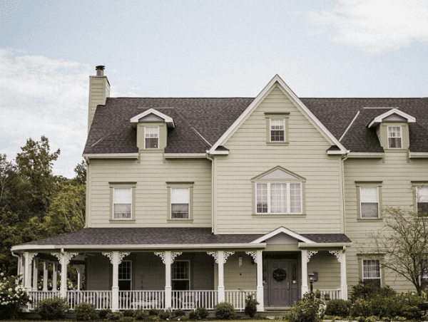 A large light green house with a porch and balcony.