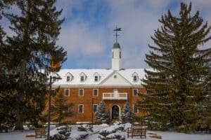 A building with snow on the roof and trees in front of it.