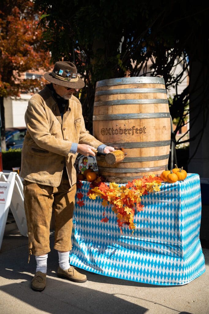 A man in brown jacket standing next to wooden barrel.
