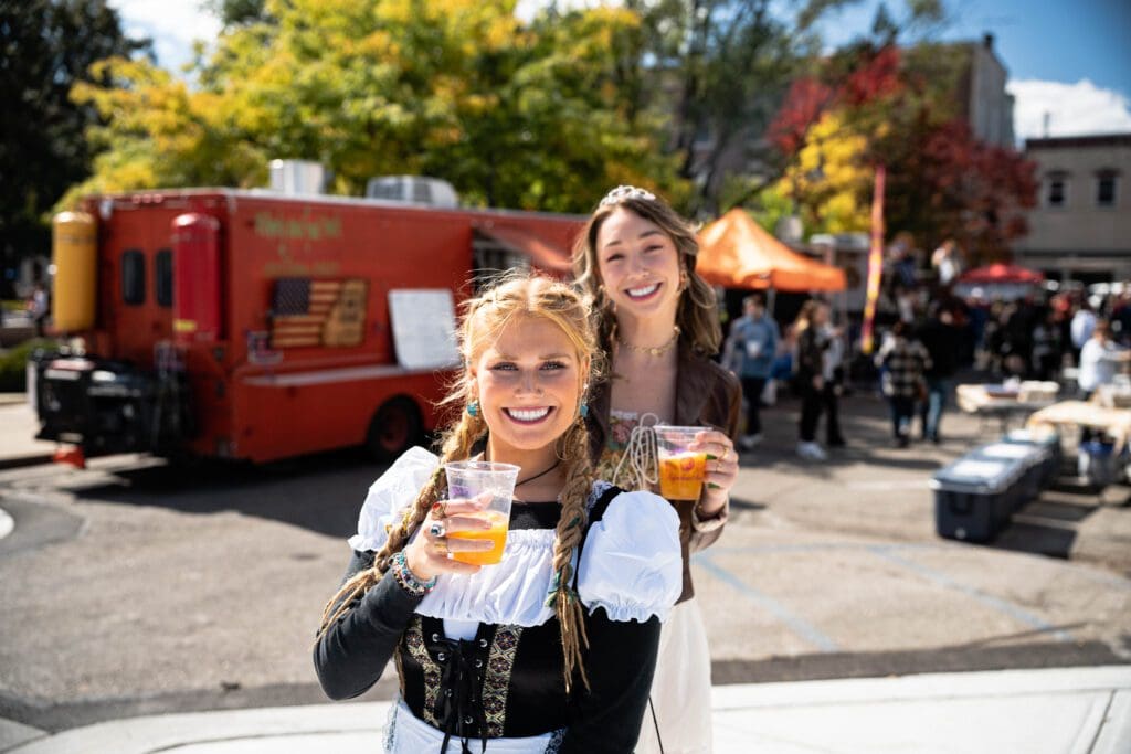 Two women holding drinks in front of a food truck.