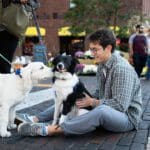 A man sitting on the ground with two dogs.