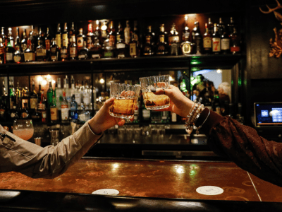 Two people holding up glasses of alcohol at a bar.