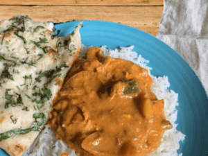 A plate of chicken tikka masala with rice and side of naan.