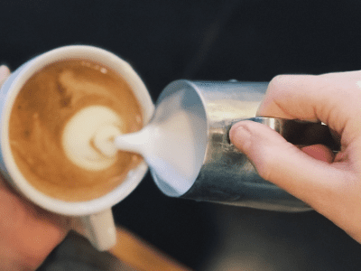 A person pouring cream into a cup of coffee.