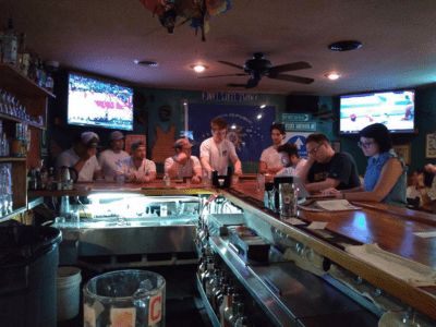 A group of people sitting at the bar watching television.