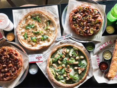 Four different pizzas on paper plates with a few toppings.