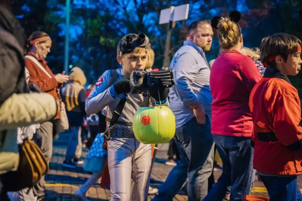 Boy in a ghostbusters costume holding a green plastic pumpkin with candy