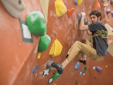 A man climbing up the side of an indoor rock wall.