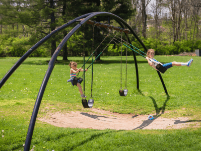 Two children swinging on a swing set in the park.
