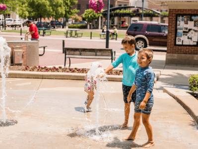 Two children playing with a water fountain in the park.