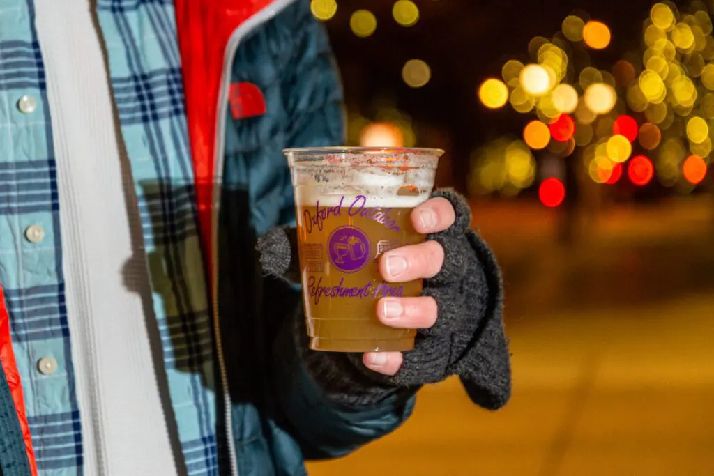 Hand holding a dora cup filled with beer, twinkle lights in the background