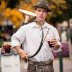 Guy wearing Oktoberfest garments with an instrument and a German beer