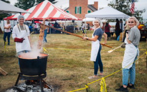 three people stirring a pot of apple butter