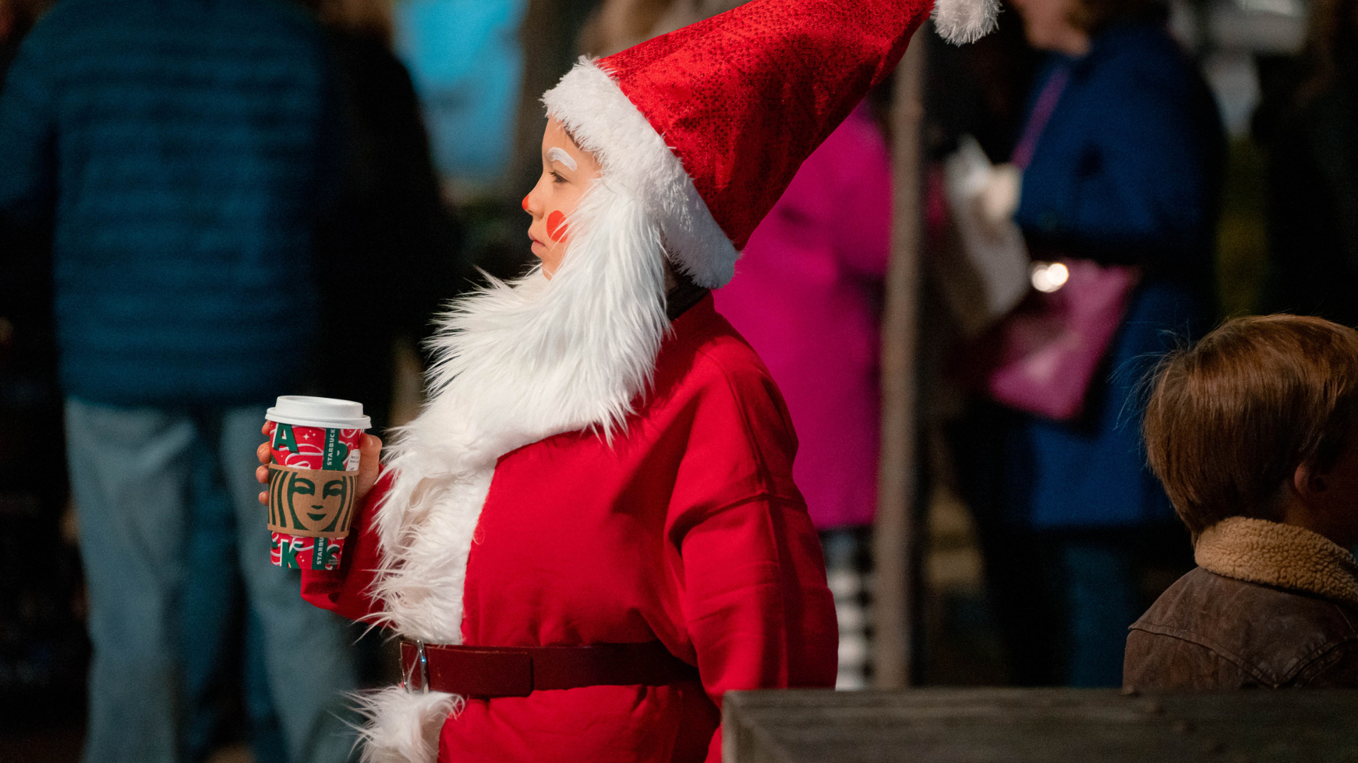 A child wearing a Santa costume holding a mug of hot cocoa