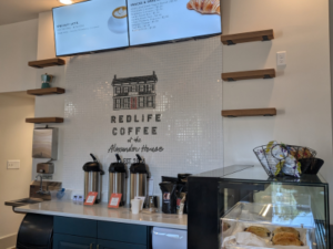 Interior of RedLife Coffee with mosaic of Alexander House and "RedLife Coffee" below two menu screens.