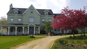 Landscape photo of the White Garden Inn with green siding and wrap around porch and red leaf tree