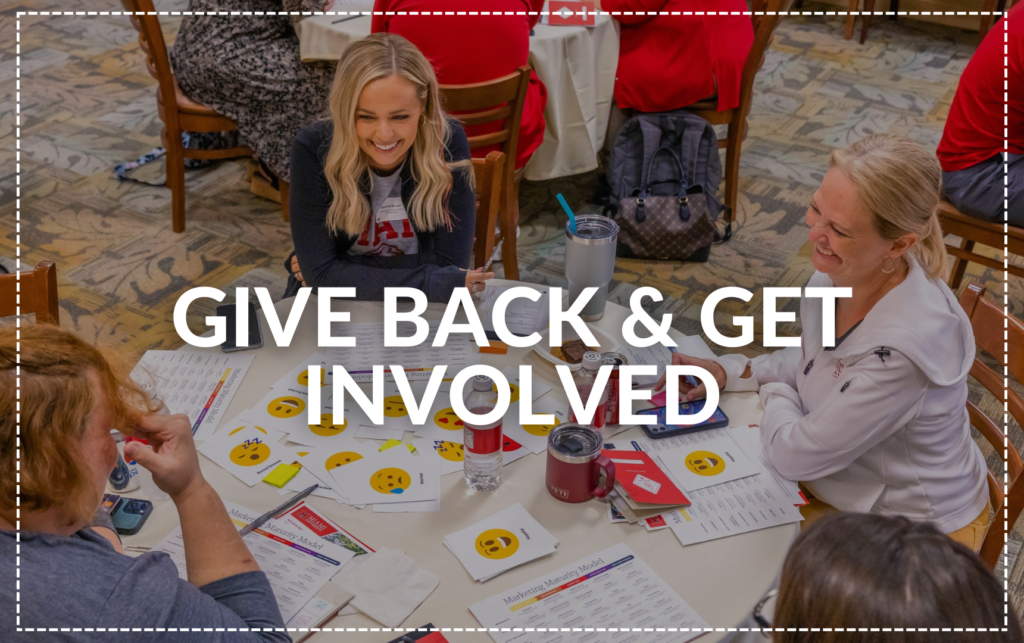 "Give Back & Get Involved" A group of people sitting at a table of worksheets.