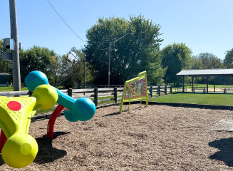 Merry Day Park with mulch substrate and interactive playground equipment and a picnic shelter in the background.