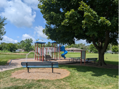 A bench nearby a playground with a slide and trees.