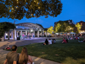 People sitting on the Oxford Memorial Park lawn in front of the pavilion at twilight