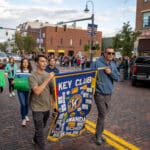 Two members of the homecoming parade hold a "Key Club" sign, while others follow behind them holding signs of their own.