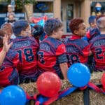 A group of young football players sits on hay bails while riding on a trailer in the Talawanda HS Homecoming parade.