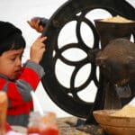 A child grinds corn using a pioneer tool.