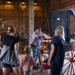 A man leans on a horse drawn carriage as he discusses it with a family.