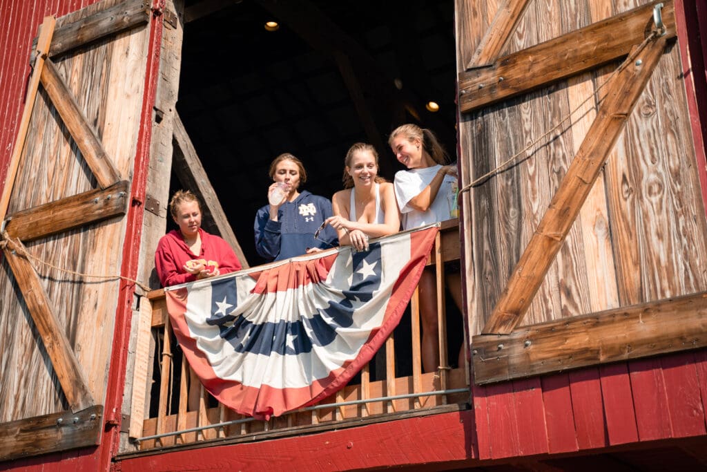 Four young ladies look down on the Apple Butter Festival from a barn loft.