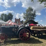 A tractor pulling a trailor with hay sits in front of some vendor tents.