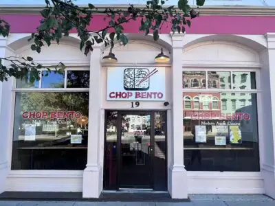 Exterior of Chop Bento with two arched windows on each side of the door with a Chop Bento box sign above.