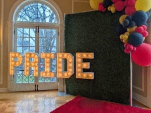 "PRIDE" lighted marquee letters in front of a beautiful window and selfie station