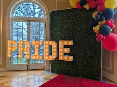 "PRIDE" lighted marquee letters in front of a beautiful window and selfie station