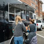 A local food vendor hands a man his order from the window of their food truck.