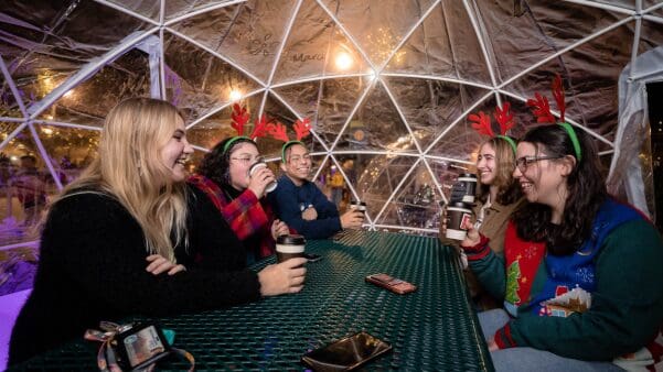 a group of young adults sitting inside a garden dome and enjoying a cup of hot cocoa
