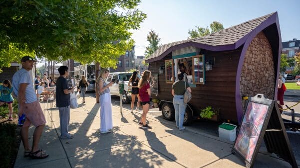 A group of people waiting in line at Ramblin Roast coffee truck stand at the Oxford Farmers Market.