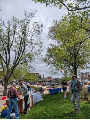 Line of Earth Fest booths at the park and people walking by.