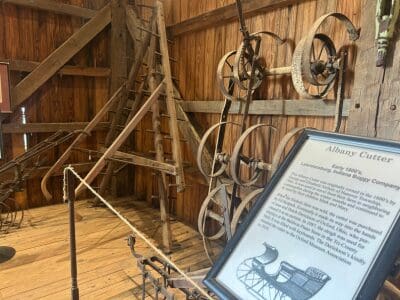 A wooden barn with old farm equipment and educational plaque.