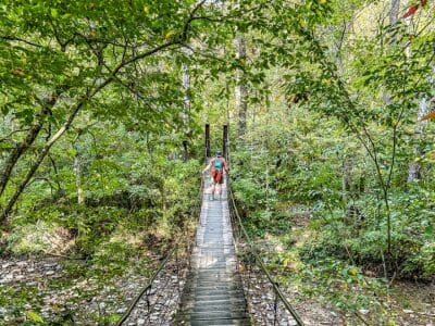 Miami Bachelor Preserve Trail there's a man walking across the wooden suspension bridge with a hiking backpack.