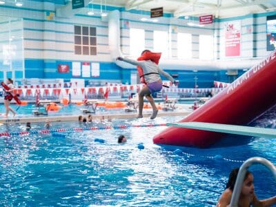 A kid with a life vest jumping off a diving board inside the Miami Rec Center pool