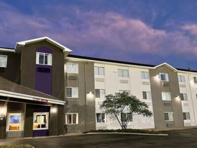 Grey and white monotone exterior of Sleep Inn hotel with carport awning and a tree